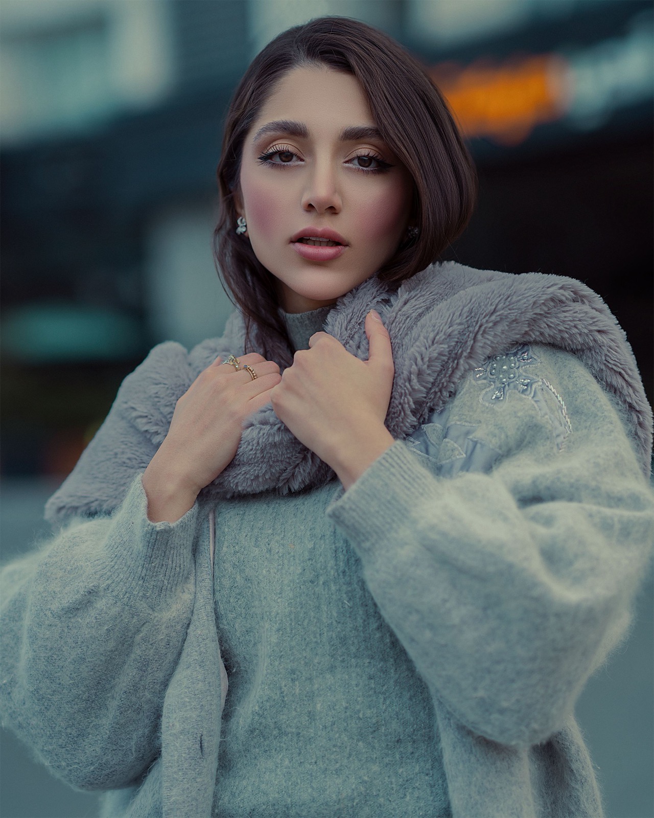 Woman wearing a pale grey coat with a thick grey scarf outdoors.