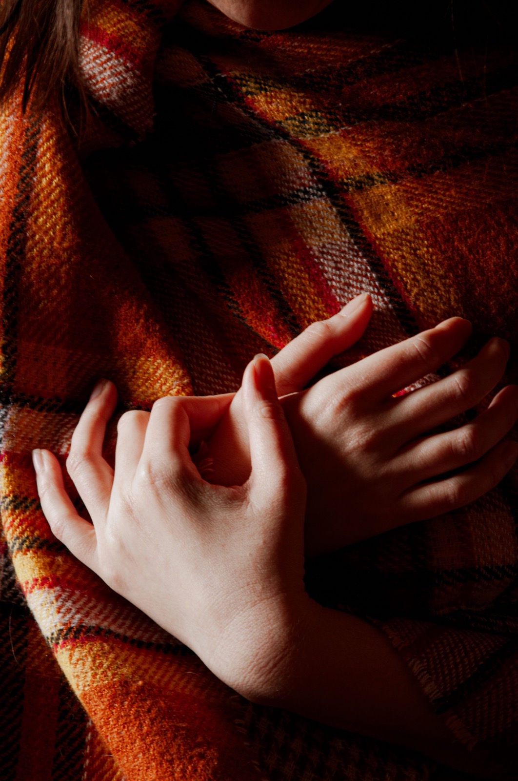 Close view of hands resting against an orange and brown checked scarf.